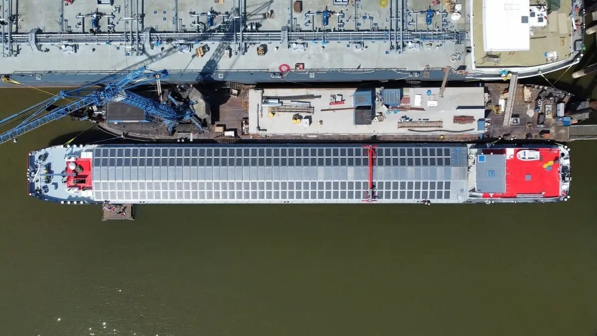 An aerial view of a barge in a dark green canal, the barge is covered in over 100 solar panels